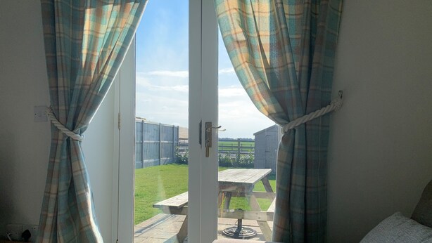 A room with a door leading to an outdoor area featuring a wooden table and a grassy lawn. - Hideaway Cottage (Halesworth)