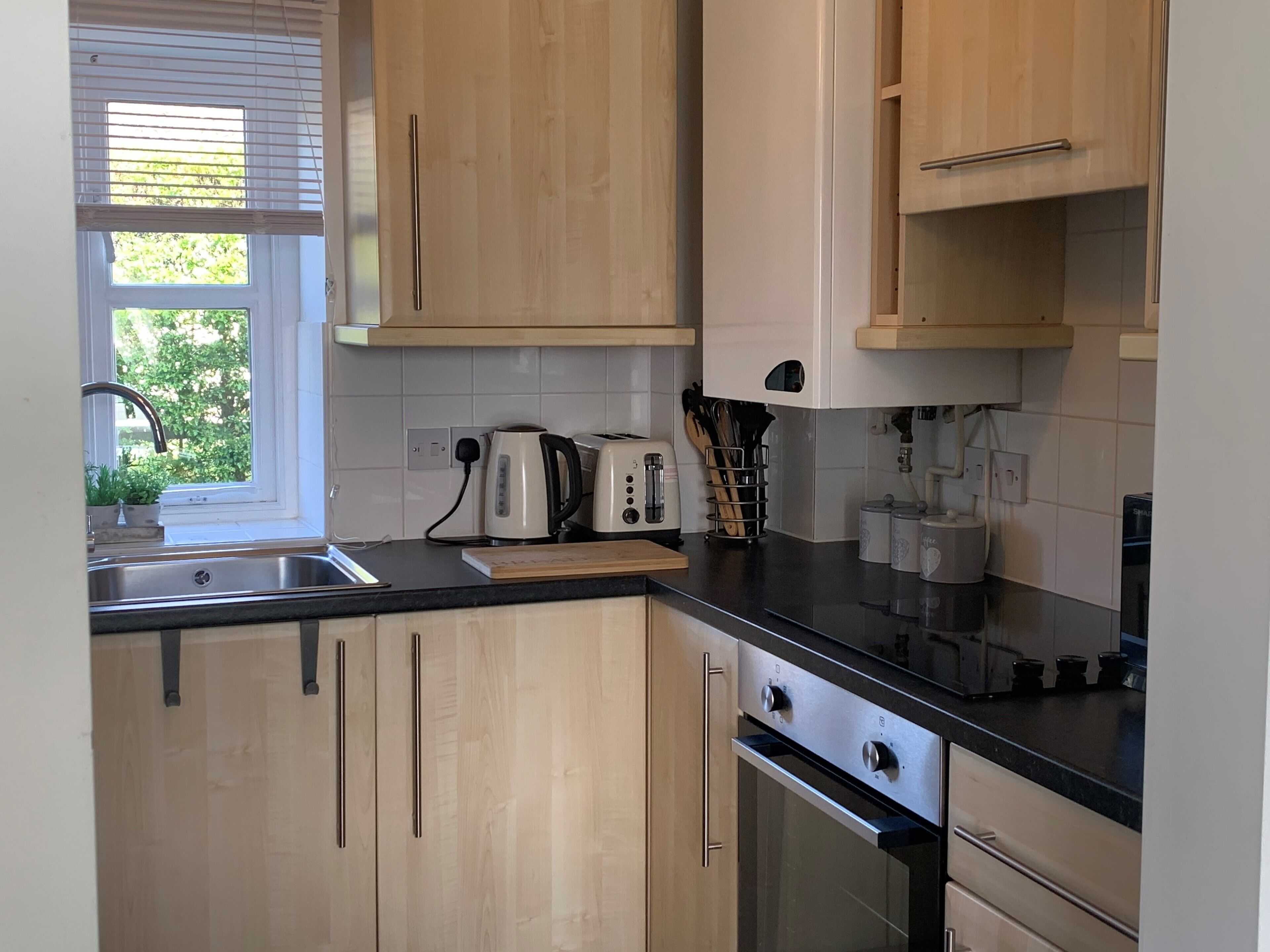 A modern kitchen with wooden cabinets, a black countertop, a built-in oven, and a window with blinds.