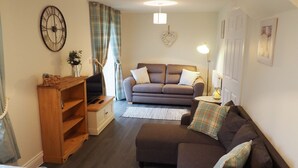 A living room with a sofa, a wooden cabinet, a television, and a heart-shaped decoration on the wall. - Hideaway Cottage (Halesworth)