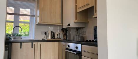 A modern kitchen with light wood cabinets, a black countertop, a kettle, a toaster, and an oven.