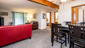 Une pièce avec un canapé rouge, des poutres en bois au plafond, une table à manger avec des chaises et un ventilateur de plafond.