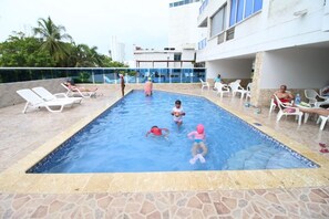 A swimming pool with children and adults around it, surrounded by lounge chairs and a building in the background. - Disfruta de la belleza de cartagena (Cartagena)