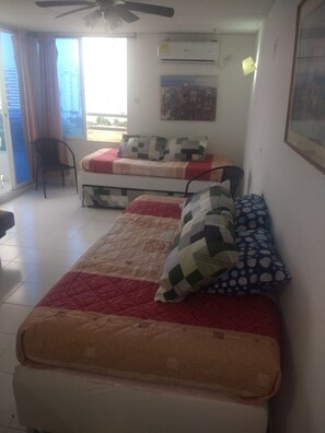 A dormitory room with two beds, a ceiling fan, an air conditioning unit, and a window with curtains. - Disfruta de la belleza de cartagena (Cartagena)