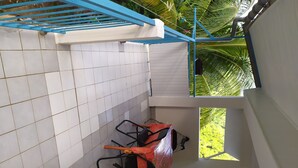 Un balcon carrelé avec une balustrade bleue, une voiture rouge garée à l’intérieur, et une vue sur des palmiers.