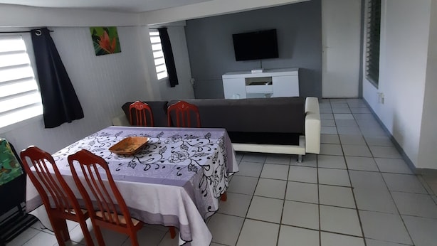 Un espace de vie compact comprenant un coin repas, un canapé, un téléviseur à écran plat et une petite kitchenette.