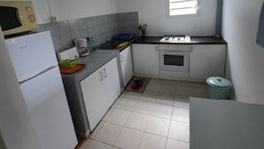 Une cuisine de taille réduite avec des meubles blancs, un four à micro-ondes, une cuisinière et une poubelle.