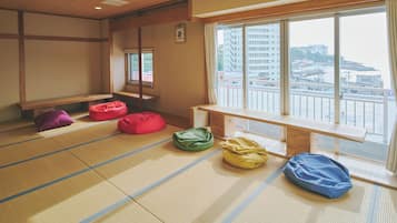 A tatami mat room with a wooden bench, tatami mats, and a view of buildings through a large window.