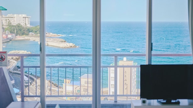 Blick durch ein Fenster auf eine Küstenstadt mit Gebäuden, einer Straße und dem Meer.