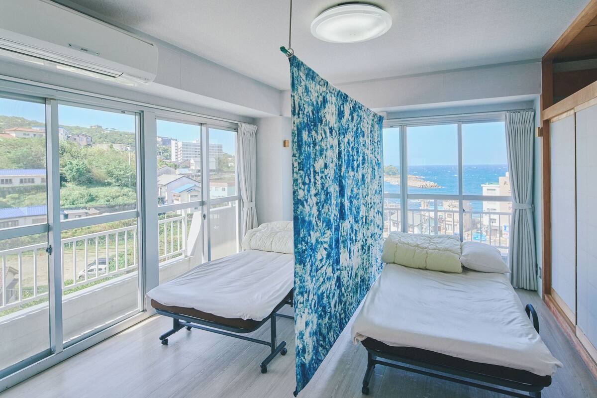 Ein Schlafzimmer mit zwei Betten, großen Fenstern und Blick auf die Stadt.