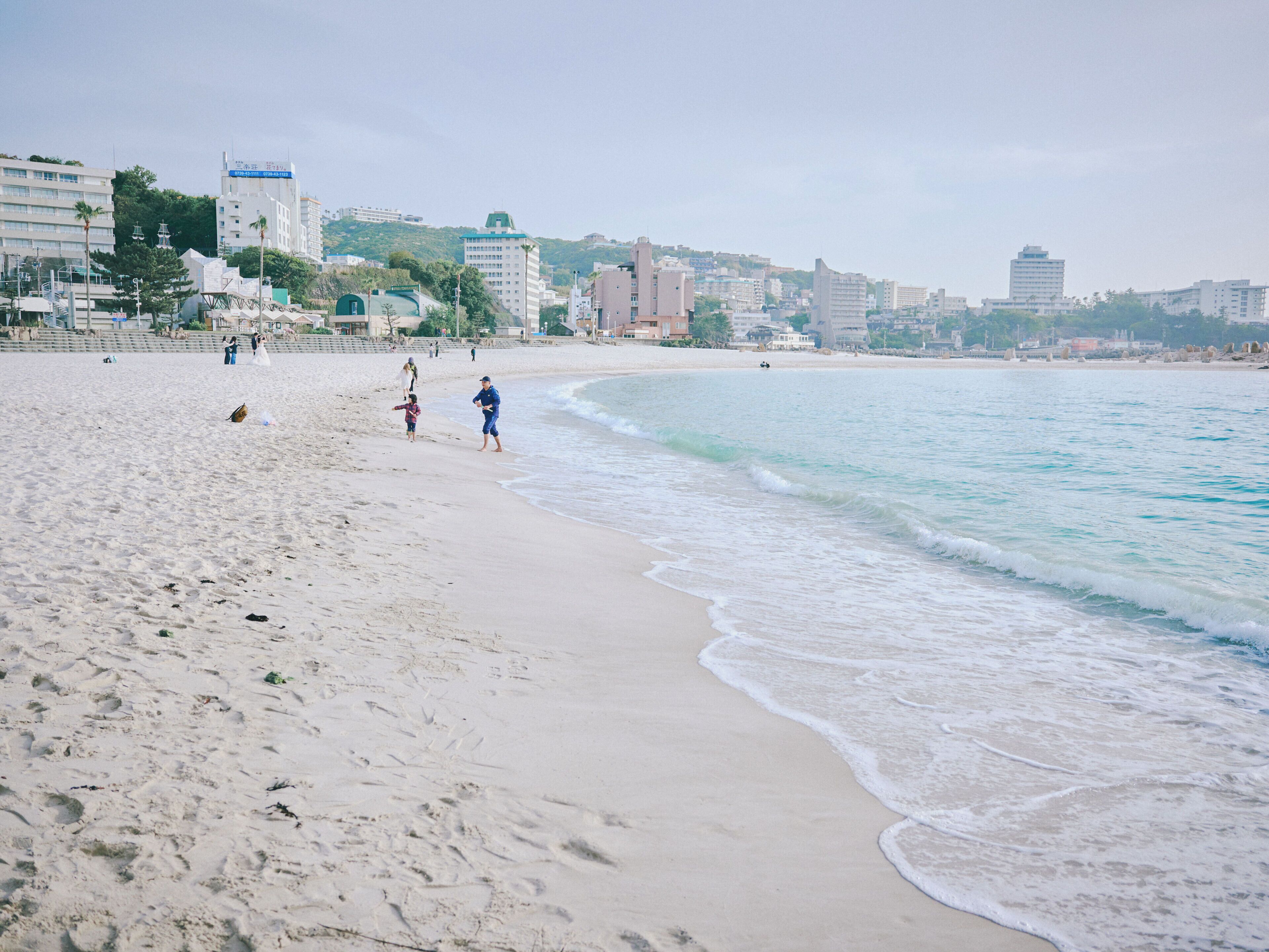 Una platja amb sorra, onades i edificis al fons.