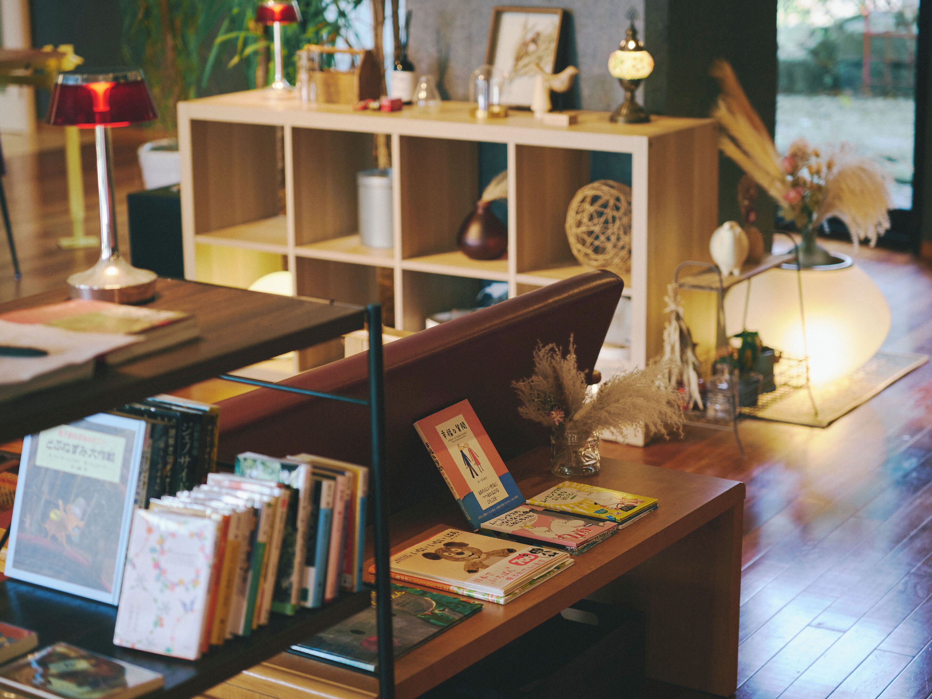Un rincón acogedor para leer con estanterías, un banco de madera y una mesa con libros y una lámpara.