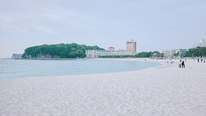 Ein Strand mit einem Hotel im Hintergrund, einem klaren Himmel und ruhiger See.