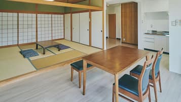 A traditional Japanese room with tatami flooring, a low wooden table, and a kitchen area visible through an open doorway.