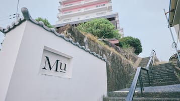 A white building with a sign reading 'Mu' and a staircase leading up to a multi-story building with balconies.