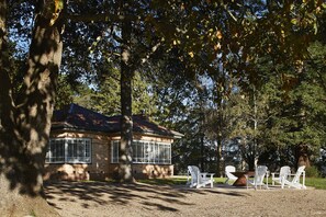 A house with a brick exterior and a large window, surrounded by trees and a gravel area with Adirondack chairs. - Polperro Farmhouse (Red Hill)