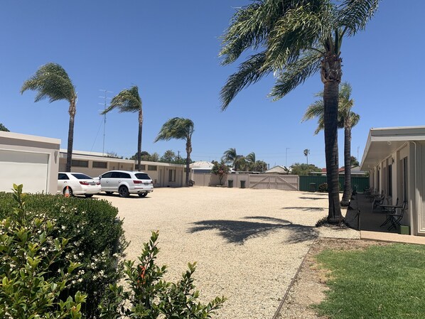 Un estacionamiento con dos coches blancos, rodeado de palmeras y un edificio con paseo techado.