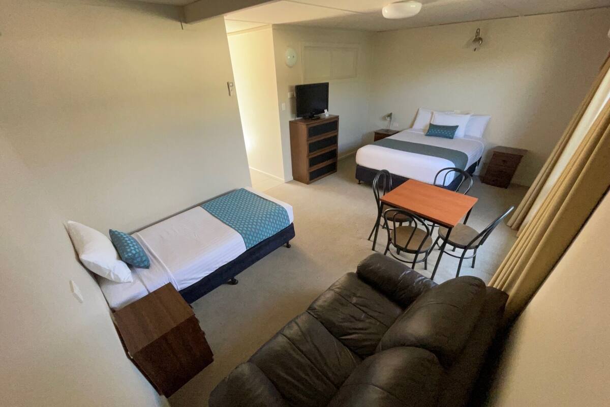 A compact room with a single bed, a small desk, a sofa, and a television.