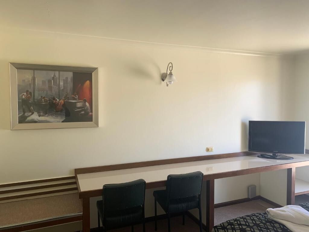 Una habitación de hotel con un escritorio, dos sillas, un televisor y un cuadro en la pared.