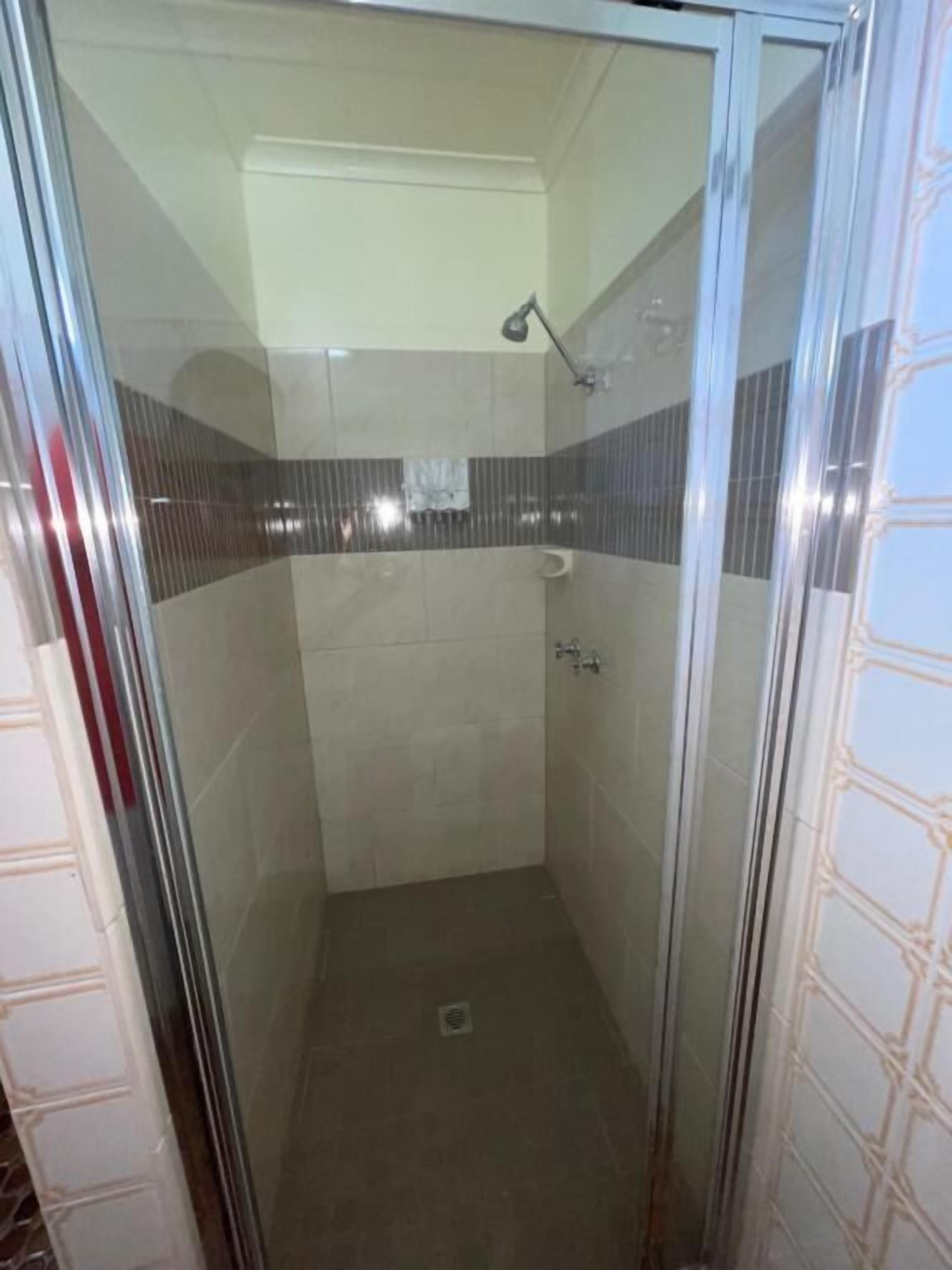 A glass-enclosed shower stall with a tiled floor and walls, a handheld showerhead, and a towel rack.