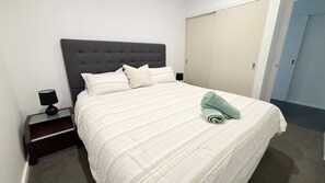 Uma cama bem arrumada com colcha listrada e travesseiros, uma luminária de cabeceira e uma toalha dobrada sobre a cama.
