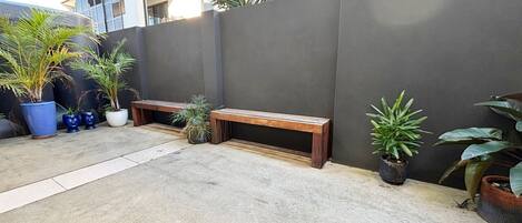 Un patio de concreto con dos bancos de madera y varias plantas en macetas.