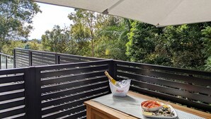 A balcony with a wooden table, a bottle of champagne, and a bowl of seafood. - Nineteen On Gregory G02 - Slow M'Ocean - Linen Supplied (SOUTH WEST ROCKS)