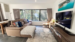 A modern living room with a sofa, a coffee table, a TV, and a large window with curtains.