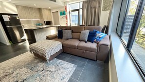 A modern living room with a sofa, ottoman, and a rug. - Nineteen On Gregory G02 - Slow M'Ocean - Linen Supplied (SOUTH WEST ROCKS)