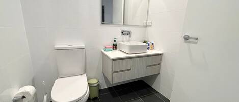 A bathroom with a toilet, a sink, a mirror, and a trash bin.