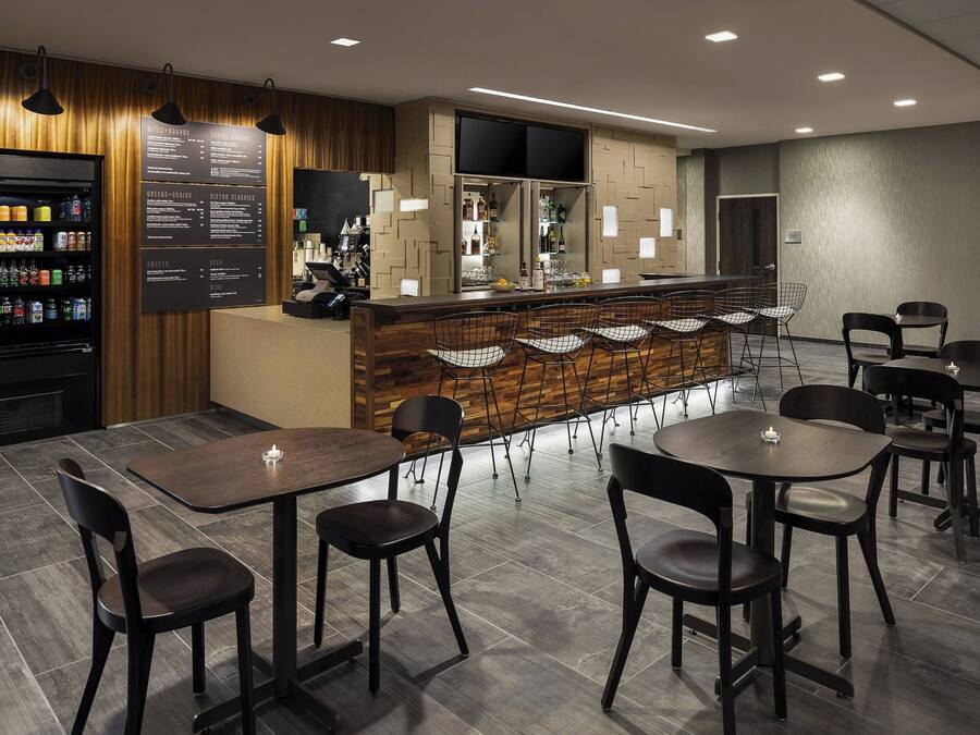 Un área de bar moderna con un tablero de menú, un dispensador de bebidas y diversas opciones de asientos.