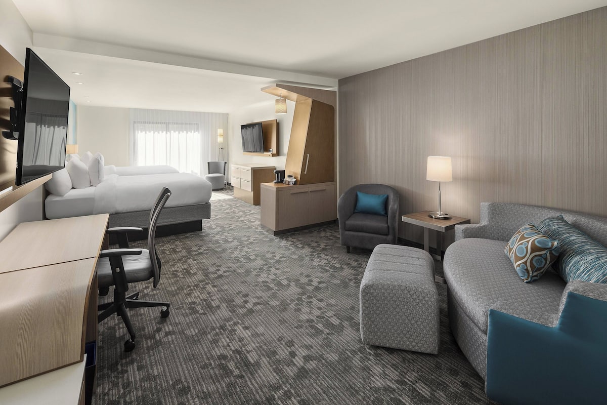 A hotel room with a bed, a sofa, a desk, a chair, a TV, and a lamp.