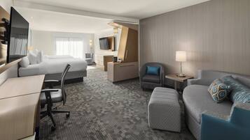 A hotel room with a bed, a sofa, a desk, a chair, a TV, and a lamp.