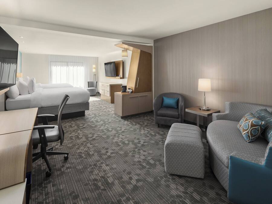A hotel room with a bed, a sofa, a desk, a chair, a TV, and a lamp.