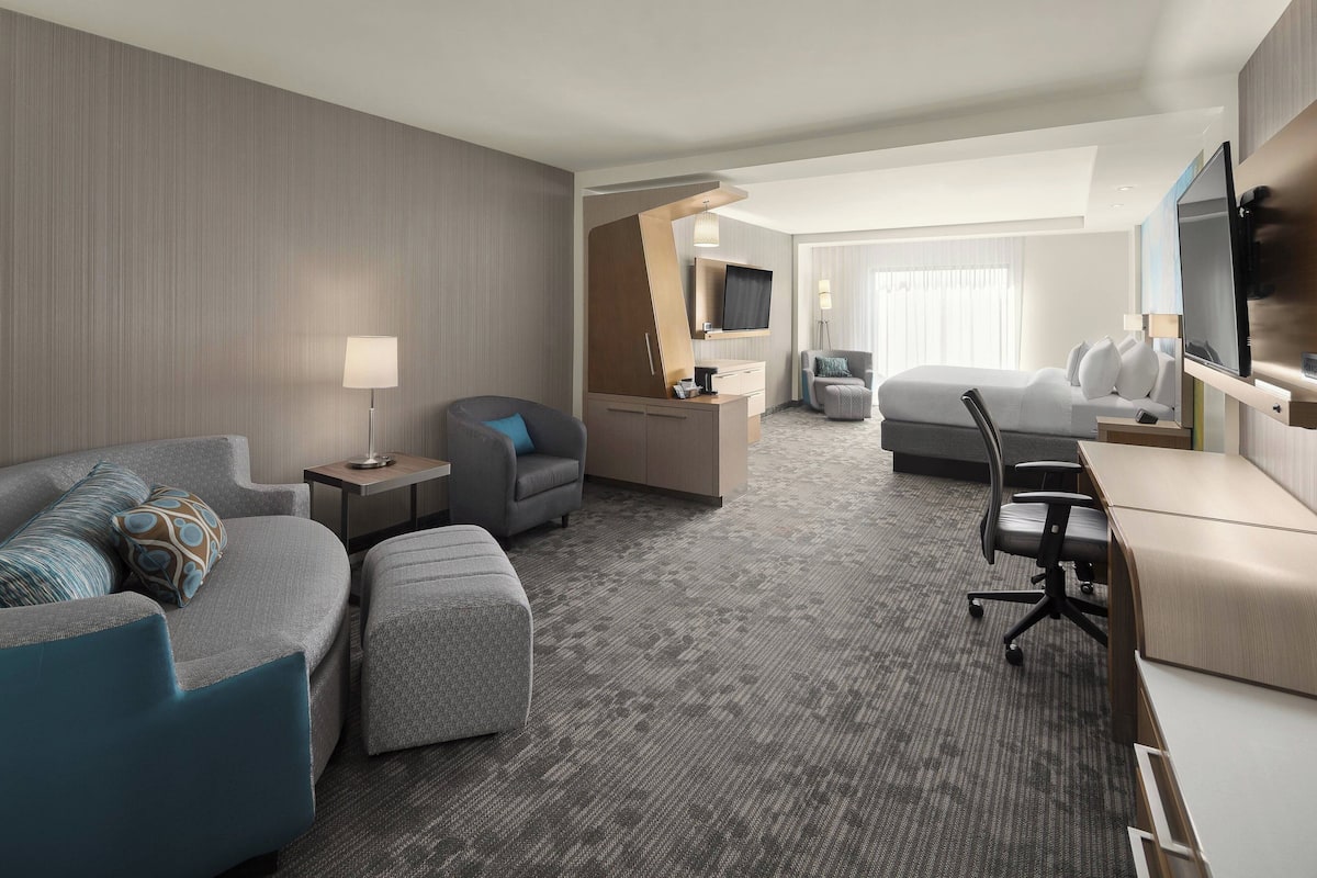 A hotel room with a sofa, armchair, desk, and a bed.