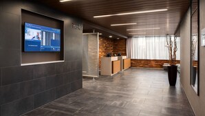 A modern hotel lobby with a digital display, a reception desk, and a wooden accent wall.