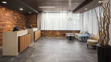 A modern reception area with a wooden wall, a reception desk, a seating area with a round table, and a large window with sheer curtains.