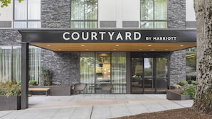 A Courtyard by Marriott hotel entrance with a covered patio area, stone facade, and seating.