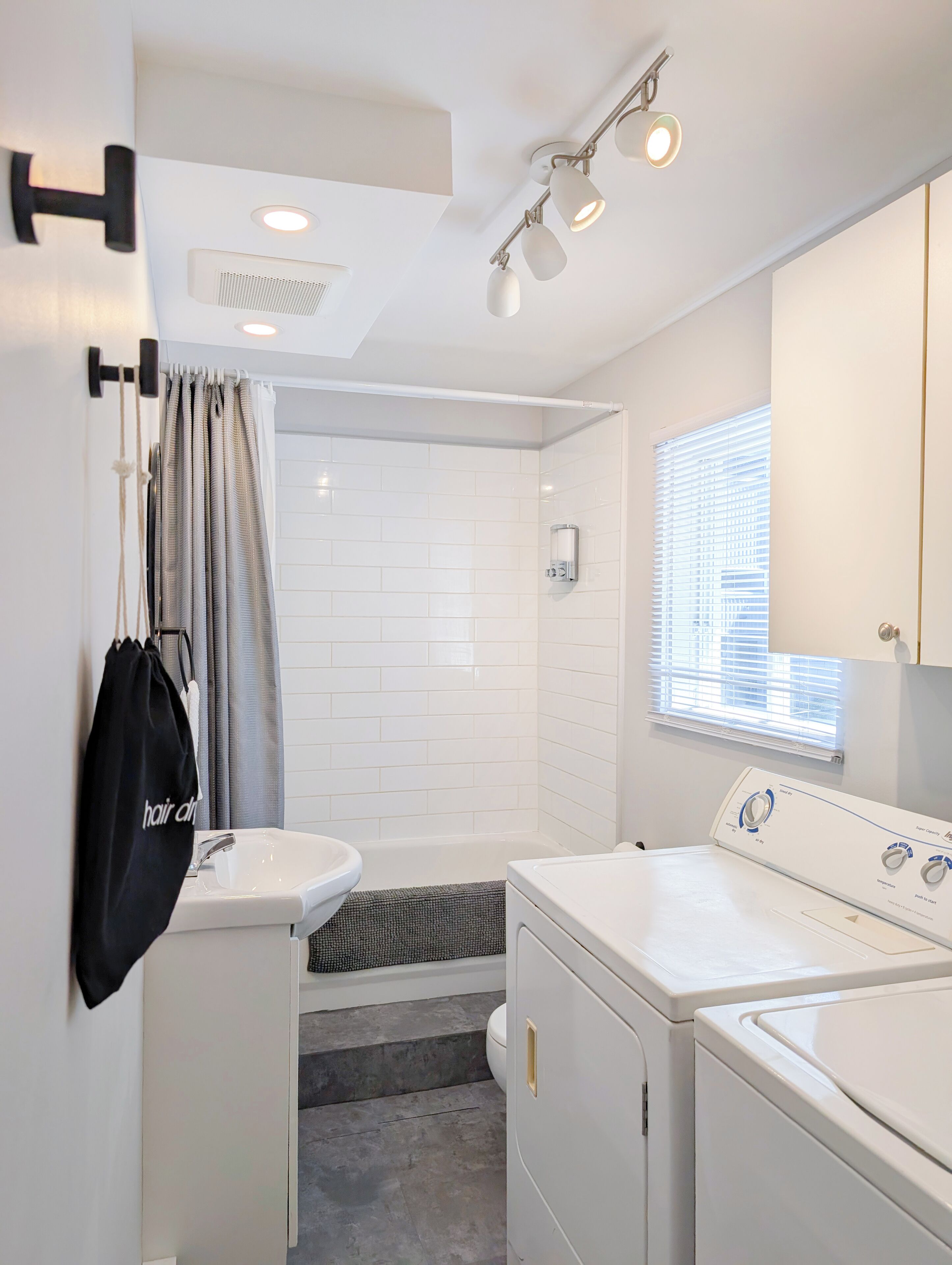 A compact, modern bathroom with a sink, toilet, shower, and laundry area.