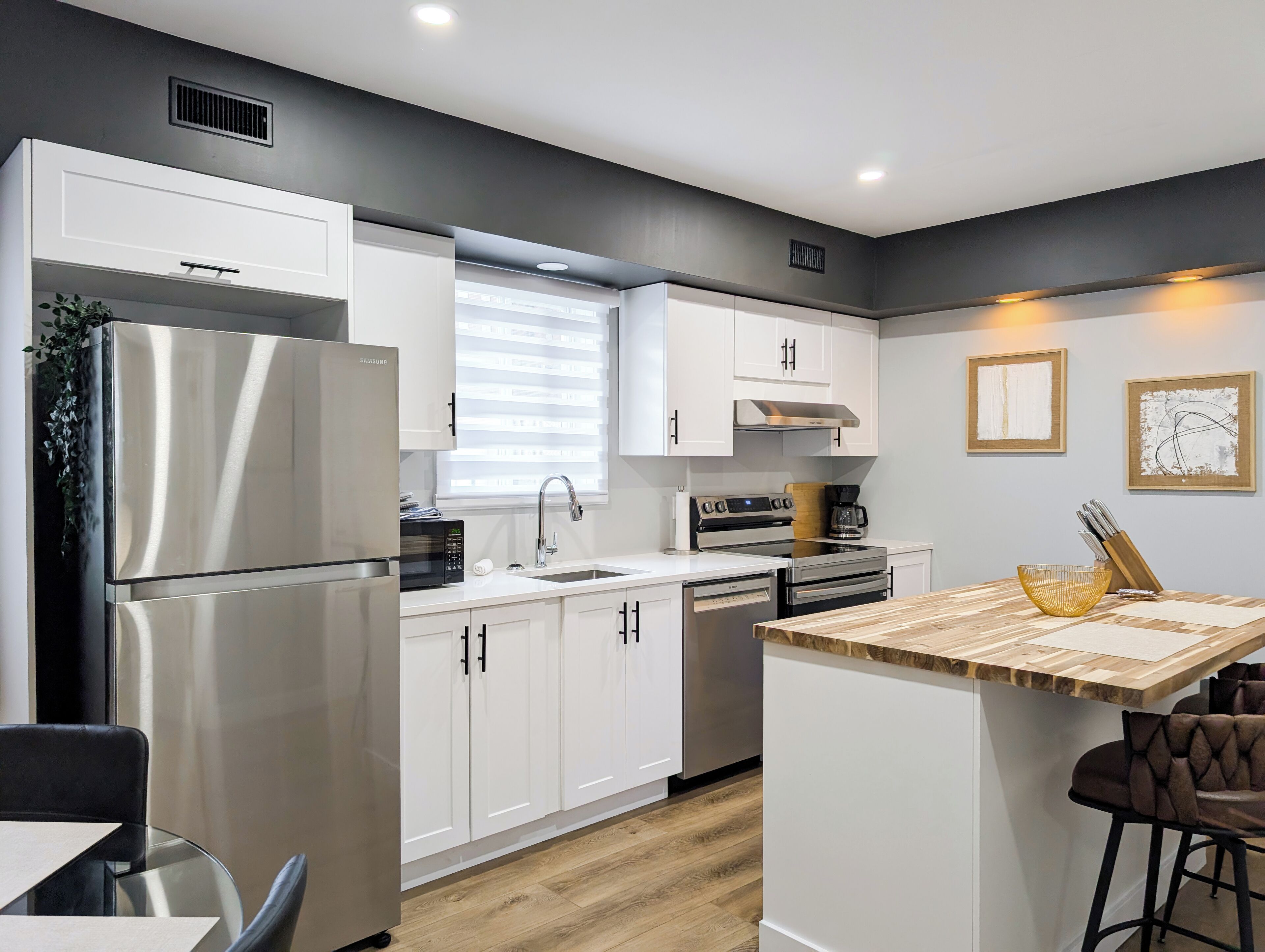 A modern kitchen with white cabinetry, stainless steel appliances, and a wooden island.