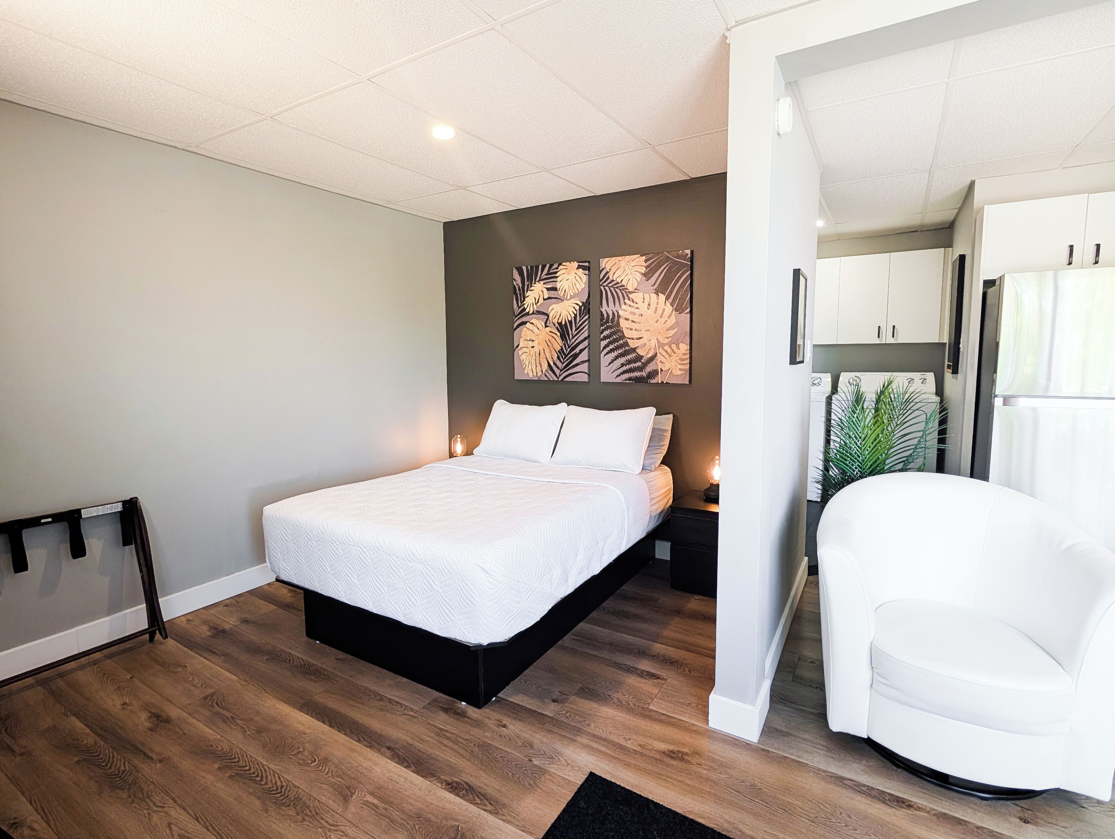 A modern bedroom with a bed, a white chair, a small table, and a wall-mounted artwork.