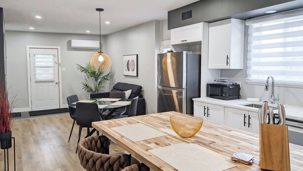 A modern kitchen with a wooden dining table, black chairs, a hanging light fixture, and a refrigerator. - Hébergement Harvey (Alma)