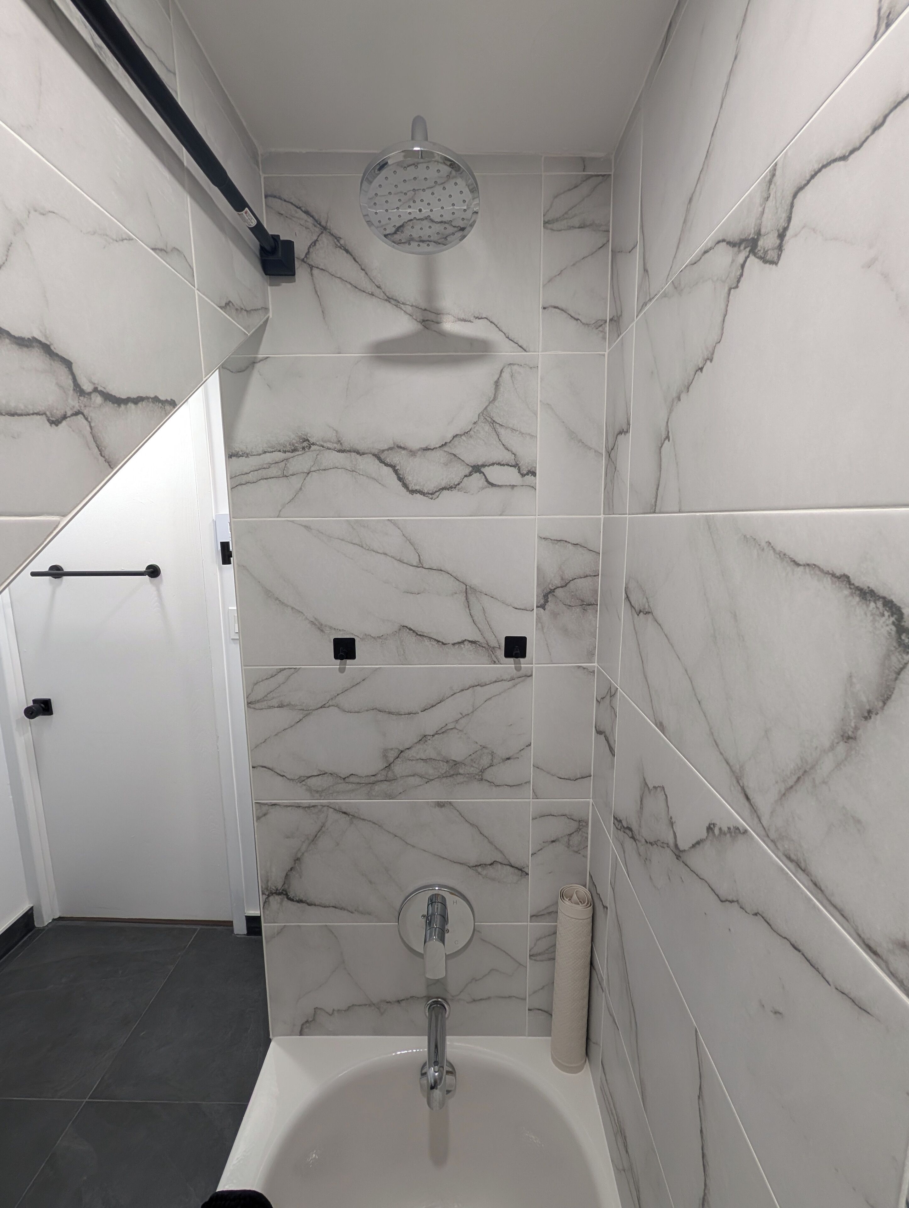 A bathroom with a bathtub, a shower head, and marble-patterned tiles.