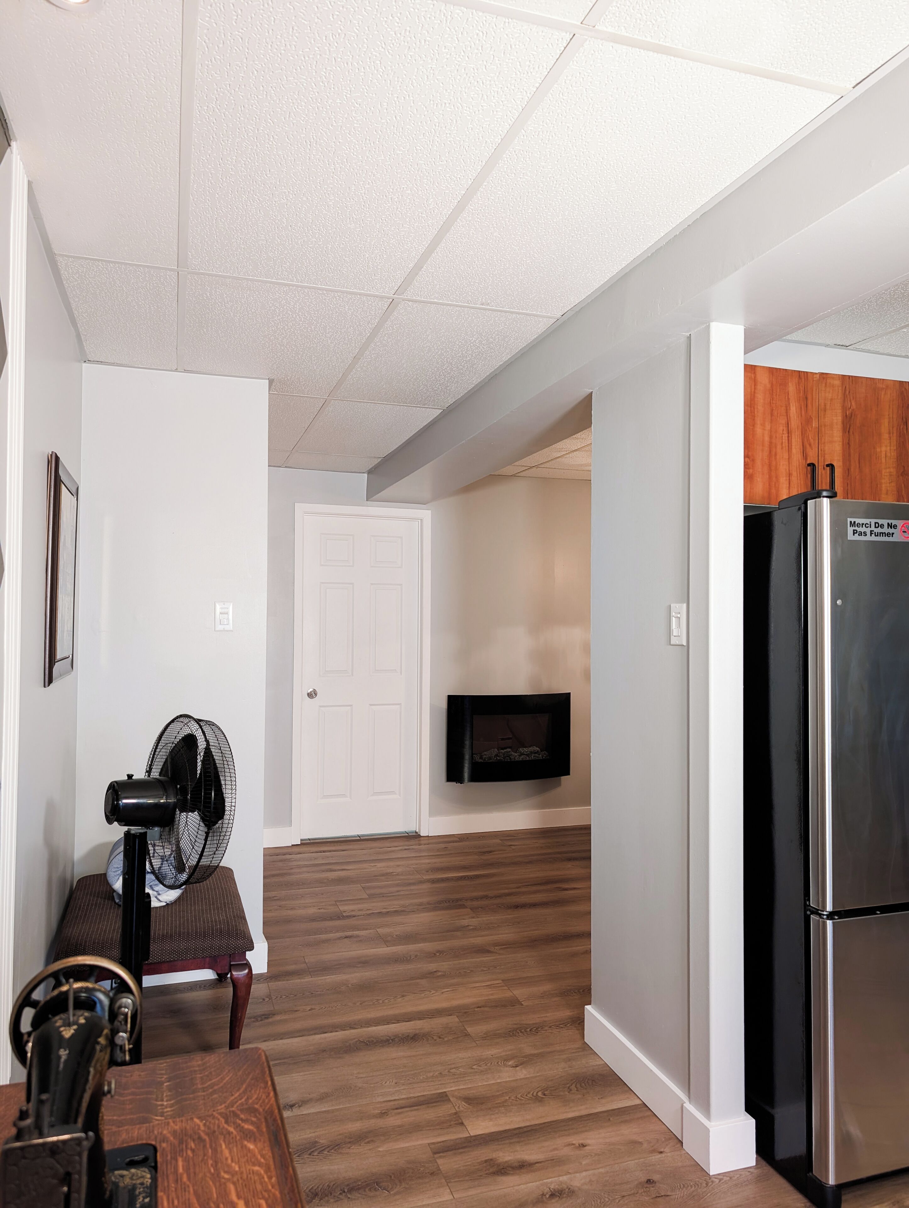 A hallway with a wooden floor, a white door, a black fan, a television mounted on the wall, and a refrigerator.