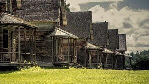 A row of wooden buildings with multiple windows and a grassy foreground. - Hébergement Harvey (Alma)