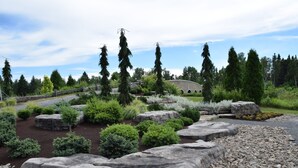 A landscaped garden with large rocks, shrubs, and trees. - Hébergement Harvey (Alma)