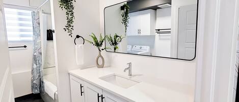 A modern bathroom with a white vanity, a large mirror, and a hanging plant.
