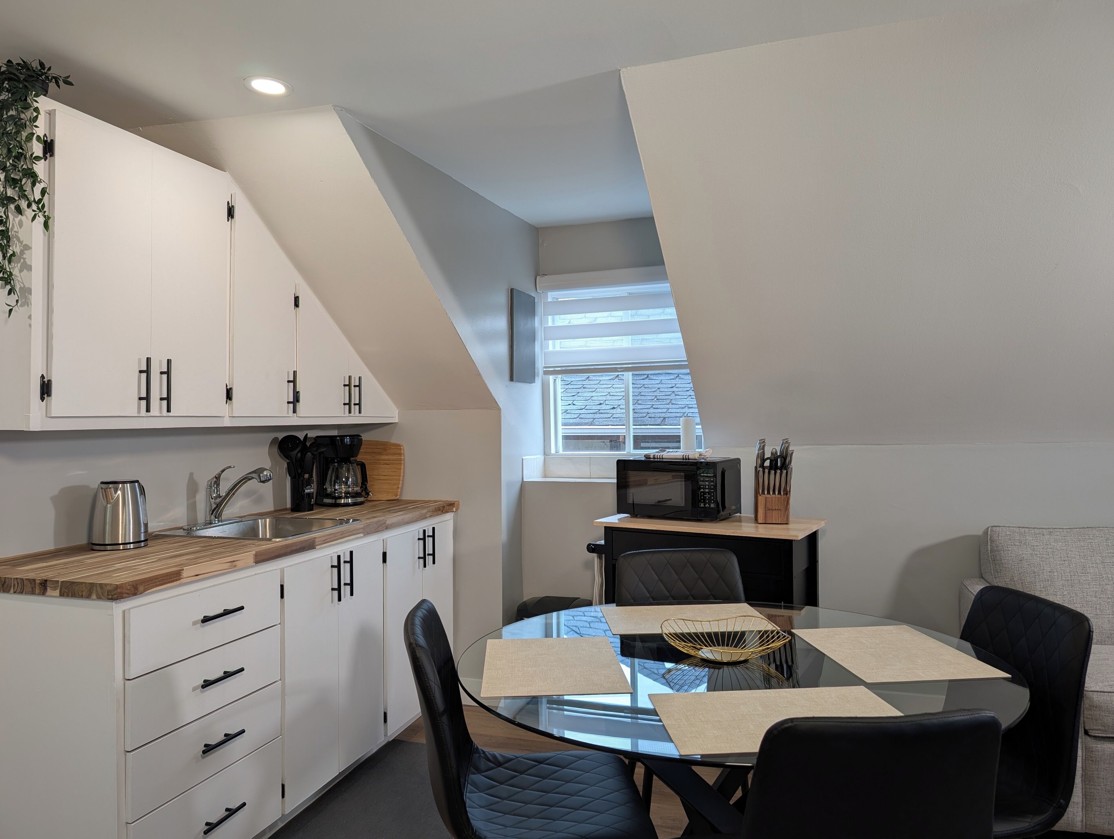 A modern kitchen with white cabinets, a wooden countertop, and a dining area with a glass table and black chairs.