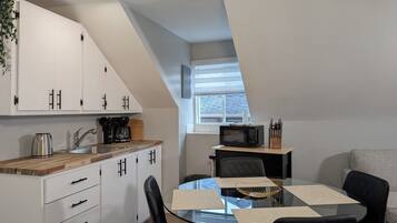 A modern kitchen with white cabinets, a wooden countertop, and a dining area with a glass table and black chairs.