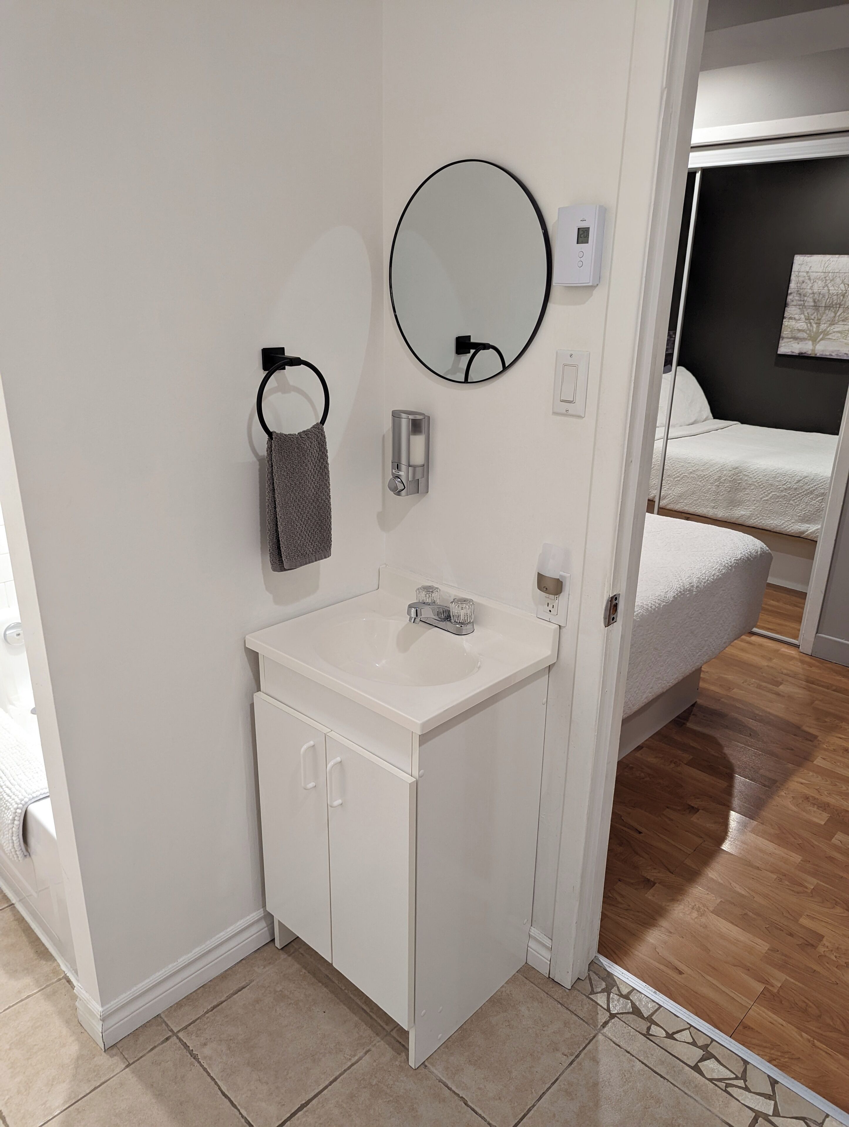 Un baño moderno con un lavamanos blanco, un espejo redondo y un perchero.