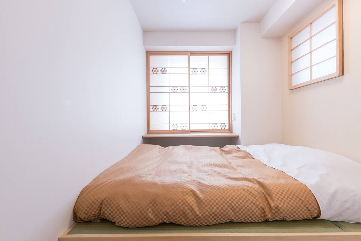 Una cama individual con una colcha a cuadros en una habitación con ventana de biombos.